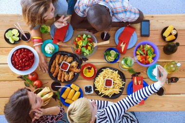 Ahşap masada otururken birlikte yemek yiyen bir grup insanın üst düzey görüntüsü. Masada yemek var. İnsanlar fast food yiyor..