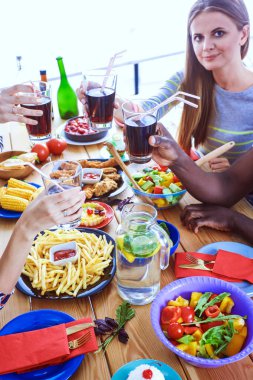 Ahşap masada otururken birlikte yemek yiyen bir grup insanın üst düzey görüntüsü. Masada yemek var. İnsanlar fast food yiyor..