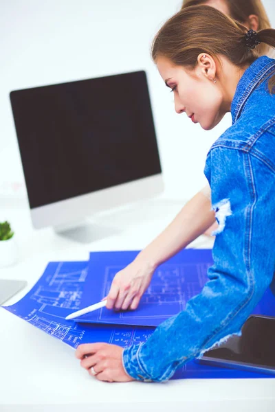 Dos mujeres jóvenes de pie cerca del escritorio con instrumentos, plan y portátil. —  Fotos de Stock