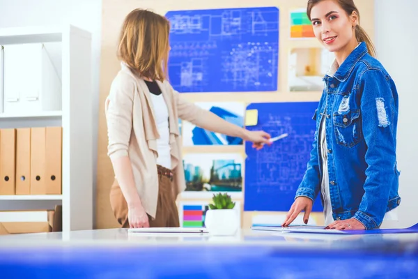 Twee jonge vrouw in de buurt van bureau met instrumenten, plan en laptop. — Stockfoto