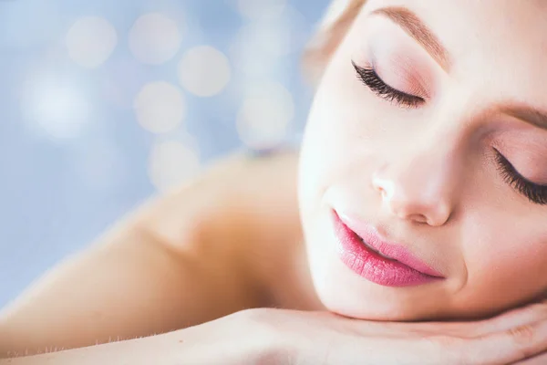 Mujer joven acostada en una mesa de masaje, relajándose con los ojos cerrados. Una mujer. Salón de spa —  Fotos de Stock