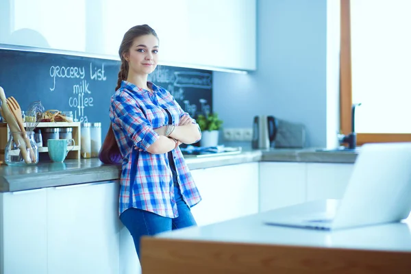 Portrait of young woman standing with arms crossed against kitchen background.
