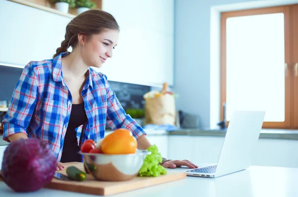 Masanın yanındaki mutfakta sebze doğrayan genç bir kadın..