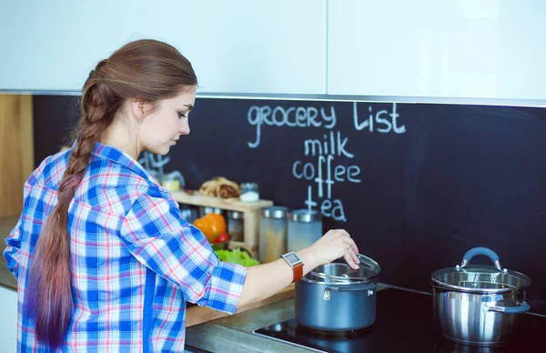Mutfakta sobanın yanında duran genç bir kadın. .