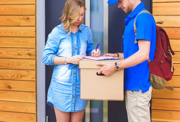 Mavi üniformalı gülümseyen kurye servis konseptine paket kutusu teslim eden teslimatçı. Mavi üniformalı gülümseyen teslimatçı.