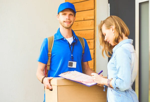 Mavi üniformalı gülümseyen kurye servis konseptine paket kutusu teslim eden teslimatçı. Mavi üniformalı gülümseyen teslimatçı.