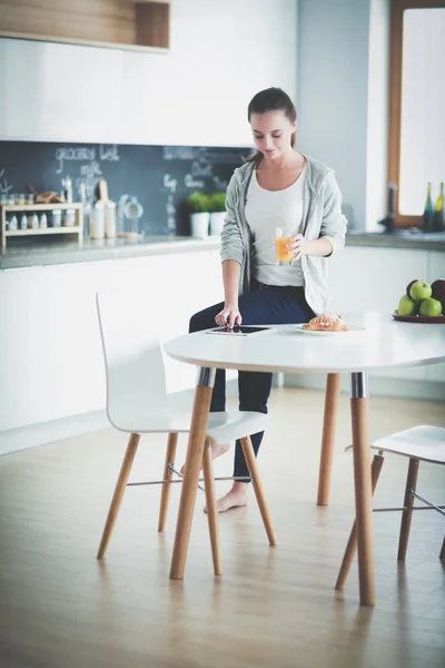 Mujer joven con jugo de naranja y tableta en la cocina. — Foto de Stock