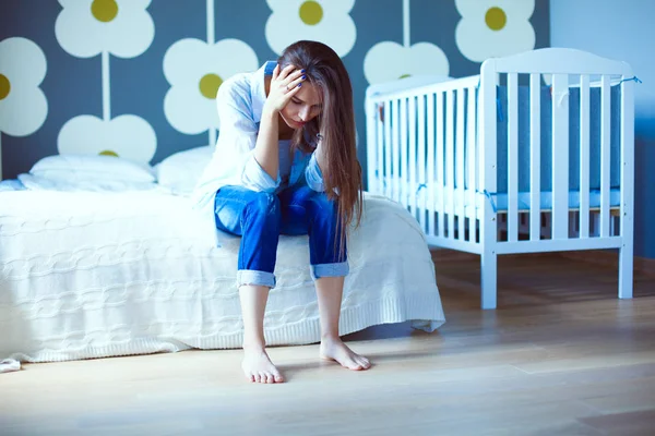 Genç çocuk karyolası yakın yatağın üstüne oturan kadın yorgun. Genç anne.