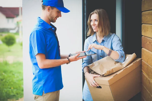 Hymyilevä postimies sinisessä univormussa toimittamassa pakettilaatikkoa vastaanottajalle kuriiripalvelun konsepti. Hymyilevä lähetti sinisessä univormussa. — kuvapankkivalokuva