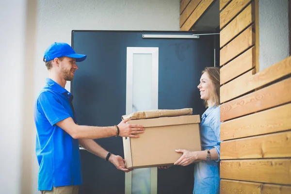 Mavi üniformalı gülümseyen kurye servis konseptine paket kutusu teslim eden teslimatçı. Mavi üniformalı gülümseyen teslimatçı.