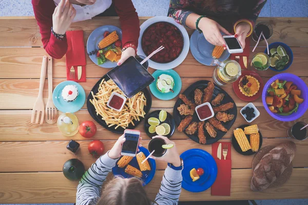 Ahşap masada otururken birlikte yemek yiyen bir grup insanın üst düzey görüntüsü. Masada yemek var. İnsanlar fast food yiyor..