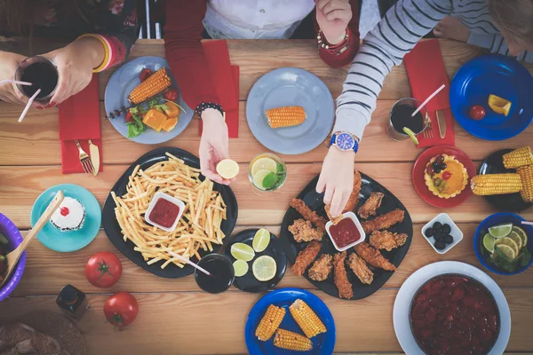 Ahşap masada otururken birlikte yemek yiyen bir grup insanın üst düzey görüntüsü. Masada yemek var. İnsanlar fast food yiyor..