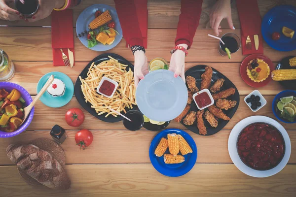 Ahşap masada otururken birlikte yemek yiyen bir grup insanın üst düzey görüntüsü. Masada yemek var. İnsanlar fast food yiyor..