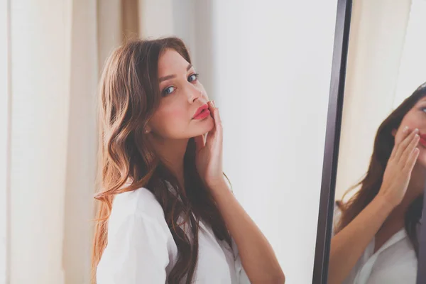 Молодая женщина смотрит на себя отражение в зеркале дома. Молодая женщина . — стоковое фото