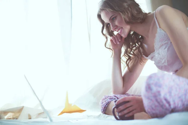 Junge schöne Frau sitzt mit Laptop im Bett. — Stockfoto
