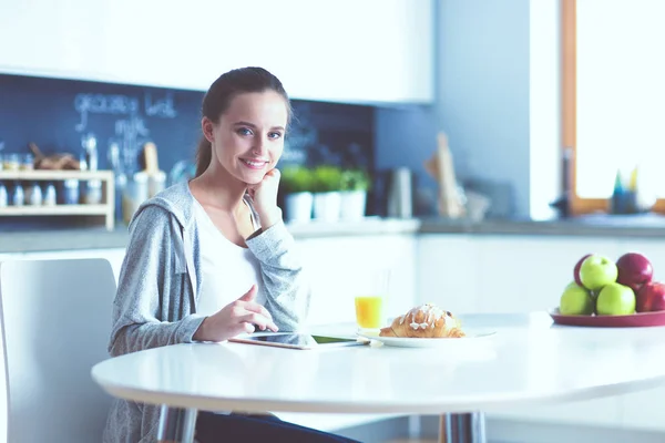 Ung kvinna med apelsinjuice och tablett i köket. — Stockfoto