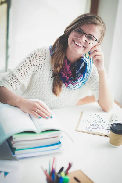 Una joven sentada en un escritorio entre libros. Estudiante —  Fotos de Stock