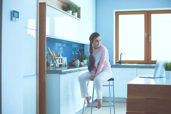 Ung kvinna sitter på bord i köket. — Stockfoto