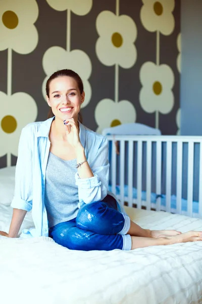 Junge Frau, die auf dem Bett neben dem Kinderbett sitzt. junge Mutter — Stockfoto