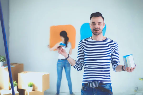 Retrato de feliz joven pareja sonriente pintando la pared interior de la casa nueva. pareja joven —  Fotos de Stock