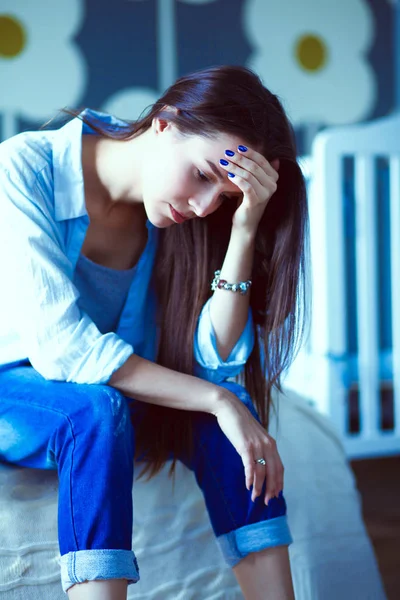 Genç çocuk karyolası yakın yatağın üstüne oturan kadın yorgun. Genç anne.