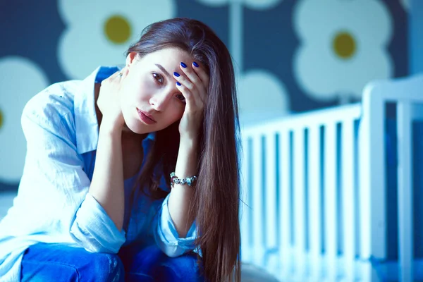 Genç çocuk karyolası yakın yatağın üstüne oturan kadın yorgun. Genç anne.
