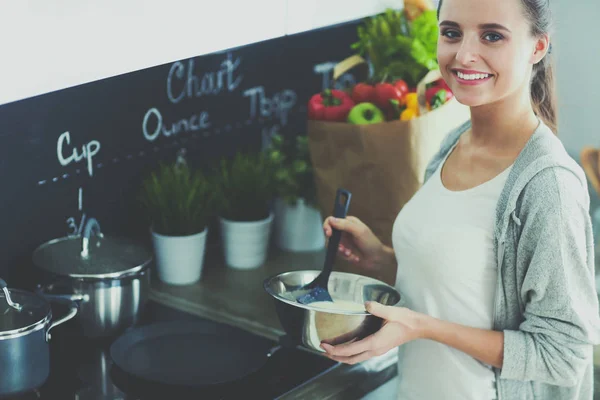 Mujer joven prepara panqueques en la cocina mientras está de pie cerca de la mesa. Mujer en la cocina. Cocinar en la cocina. — Foto de Stock