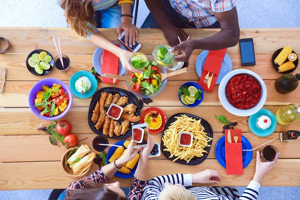 Top view of group of people having dinner together while sitting at wooden table. Food on the table. People eat fast food. — Stock Photo, Image