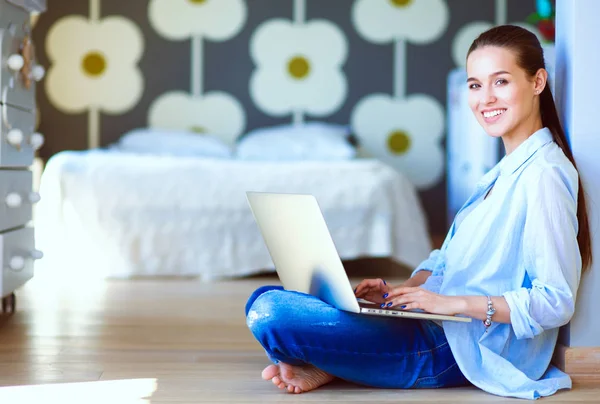 Ung kvinna som sitter på golvet nära barnens babysäng med laptop. Ung mamma — Stockfoto