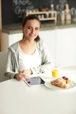 Mutfakta portakal suyu ve tableti olan genç bir kadın..