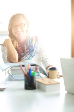 Kitapların arasında bir masada oturan genç bir kadın. Öğrenci