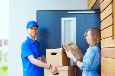 Mavi üniformalı gülümseyen kurye servis konseptine paket kutusu teslim eden teslimatçı. Mavi üniformalı gülümseyen teslimatçı.