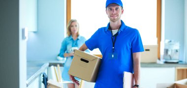 Mavi üniformalı gülümseyen kurye servis konseptine paket kutusu teslim eden teslimatçı.