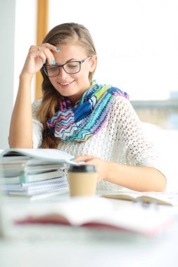 Kitapların arasında bir masada oturan genç bir kadın. Öğrenci