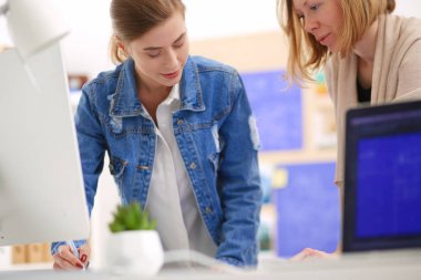 Masanın yanında duran iki genç kadın enstrüman, plan ve dizüstü bilgisayarla.