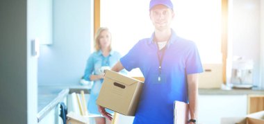 Mavi üniformalı gülümseyen kurye servis konseptine paket kutusu teslim eden teslimatçı.