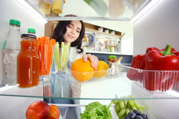 Sağlıklı yiyecek, sebze ve meyvelerle dolu açık buzdolabının yanında duran kadın portresi. Kadın portresi