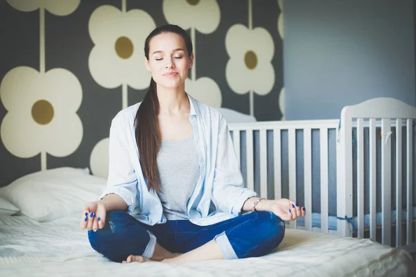 Young woman sitting on the bed near childrens cot. Young mom — Stock Photo, Image