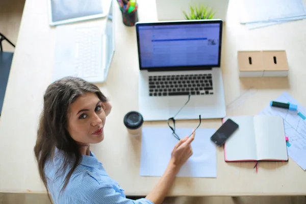 Egy fiatal nő ül az irodai asztalnál, a laptop képernyőjét bámulja. Fiatal nő — Stock Fotó