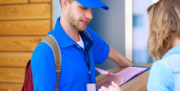 Uomo di consegna sorridente in uniforme blu che consegna pacchi al destinatario - concetto di servizio di corriere — Foto Stock