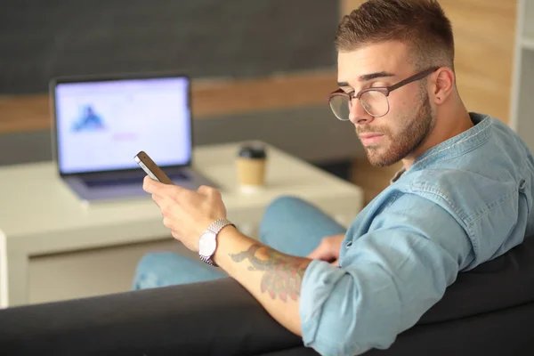 Jonge man met telefoon en werkt op de laptop. — Stockfoto