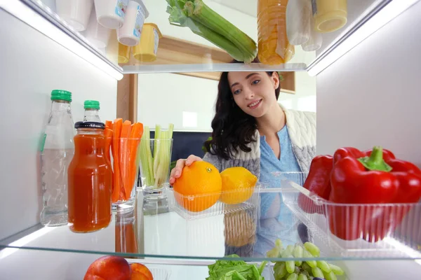 Retrato de una mujer parada cerca de una nevera abierta llena de alimentos saludables, verduras y frutas. Retrato de mujer — Foto de Stock