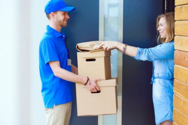 Mavi üniformalı gülümseyen kurye servis konseptine paket kutusu teslim eden teslimatçı. Mavi üniformalı gülümseyen teslimatçı.