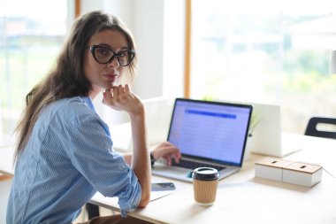Ofis masasında oturan genç bir kadın dizüstü bilgisayar ekranına bakıyor. Genç kadın.
