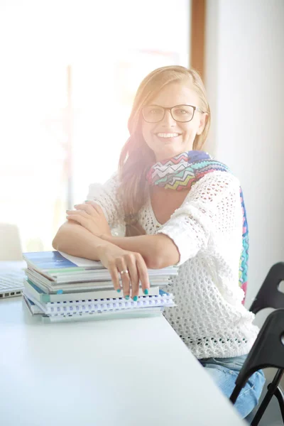 Ung kvinna som sitter vid ett skrivbord bland böcker. Studerande — Stockfoto