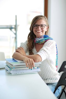 Kitapların arasında bir masada oturan genç bir kadın. Öğrenci
