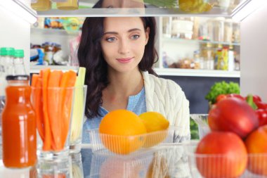 Sağlıklı yiyecek, sebze ve meyvelerle dolu açık buzdolabının yanında duran kadın portresi. Kadın portresi