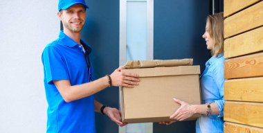 Mavi üniformalı gülümseyen kurye servis konseptine paket kutusu teslim eden teslimatçı.