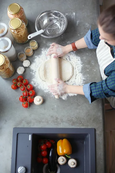 Güzel bir kadın mutfakta pasta pişiriyor. Masanın yanında duruyor..