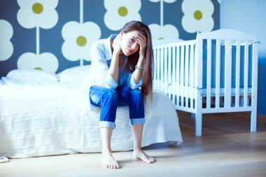 Genç çocuk karyolası yakın yatağın üstüne oturan kadın yorgun. Genç anne.